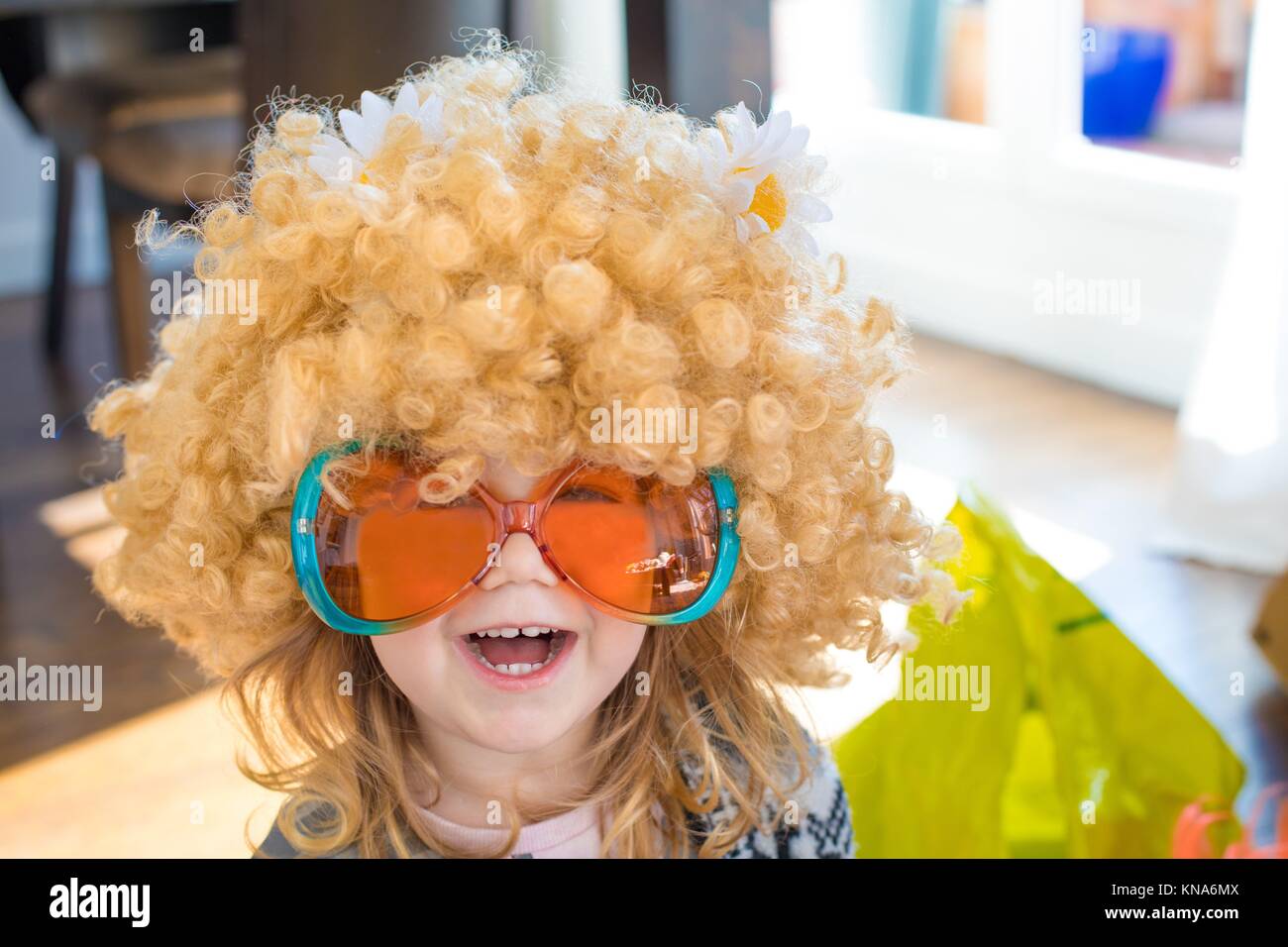 Gracioso retrato de tres años de edad, disfrazado de sesenta, con gran  peluca rubia cabellera rizada con daisy flores en la cabeza, con naranja y  verde Fotografía de stock - Alamy
