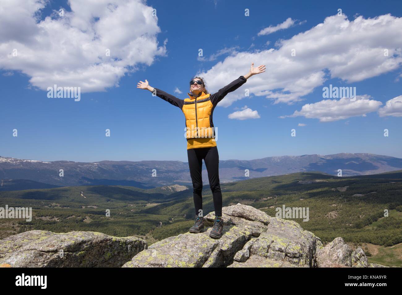 Deporte De Senderismo O Trekking Mujer Con Chaqueta De Color Púrpura,  Sentado En El Pico De La Roca, Escribiendo Teléfono Inteligente Móvil,  Detrás Del Valle De Lozoya Y El Parque Guadarrama, En