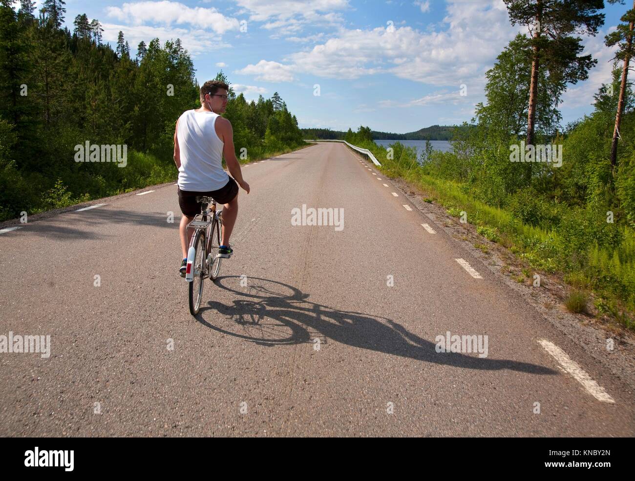 Hombre montando bicicleta en la carretera, el paisaje del norte de Suecia. Foto de stock