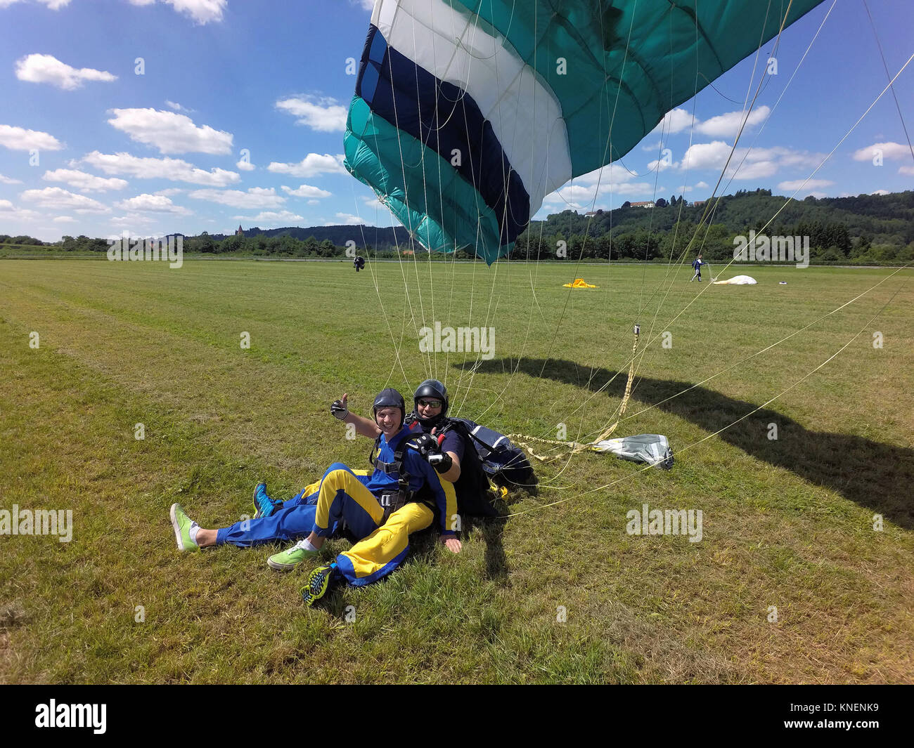 Retrato del tándem paracaidistas dando pulgares para arriba después del aterrizaje de campo Foto de stock