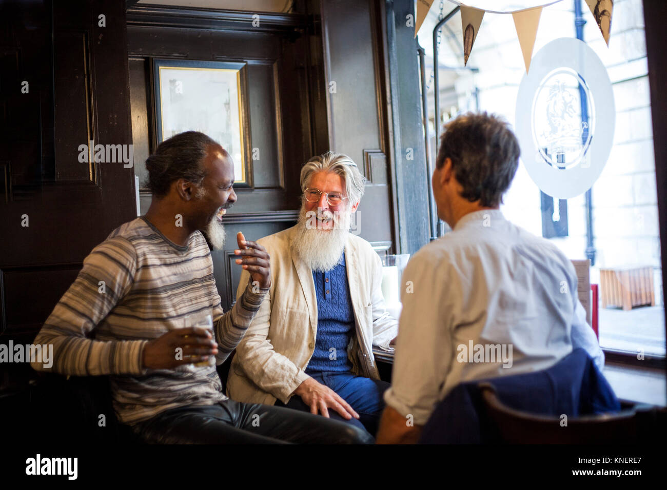 Tres hombres maduros, sentados juntos en el pub hablando Foto de stock