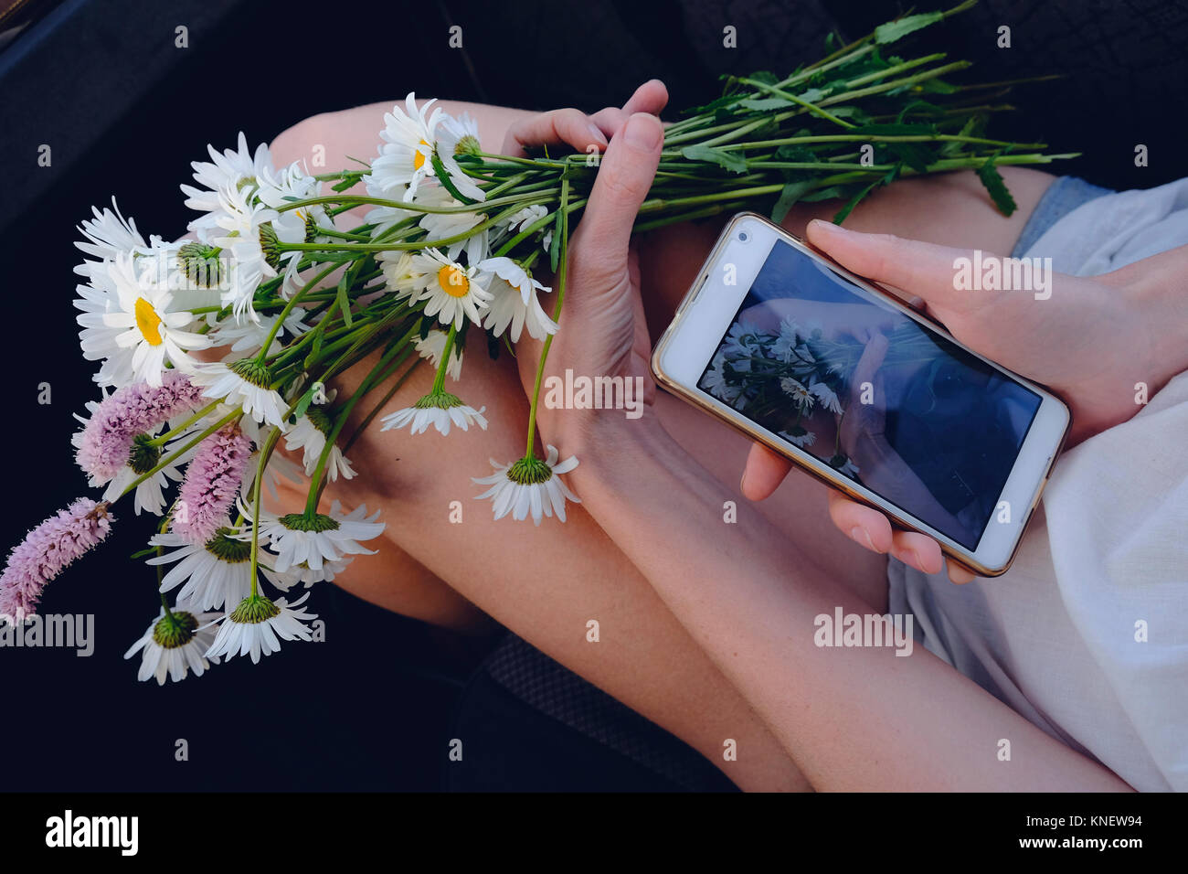 Mujer sosteniendo flores frescas, tomando la fotografía de flores, utilizando el smartphone, close-up Foto de stock