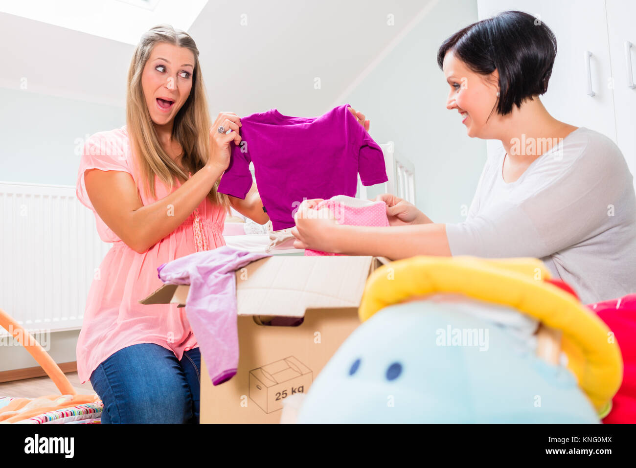 La mujer embarazada y el amigo compartir ropa de bebé Foto de stock