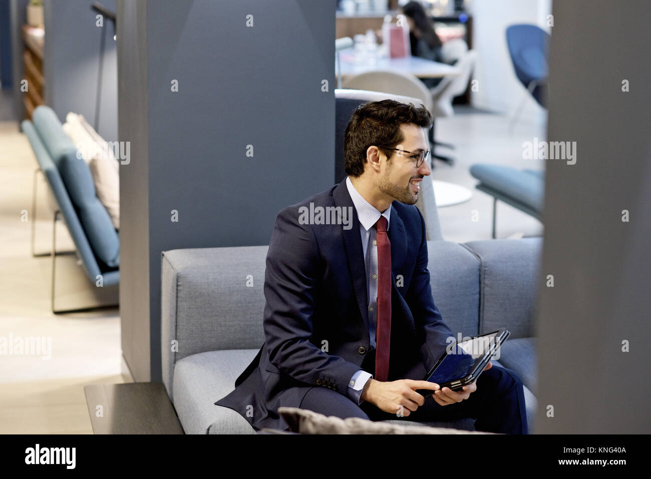 El empresario latino vestida con un traje inteligente sosteniendo un dispositivo Tablet móvil en una oficina de diseño interior contemporáneo Foto de stock