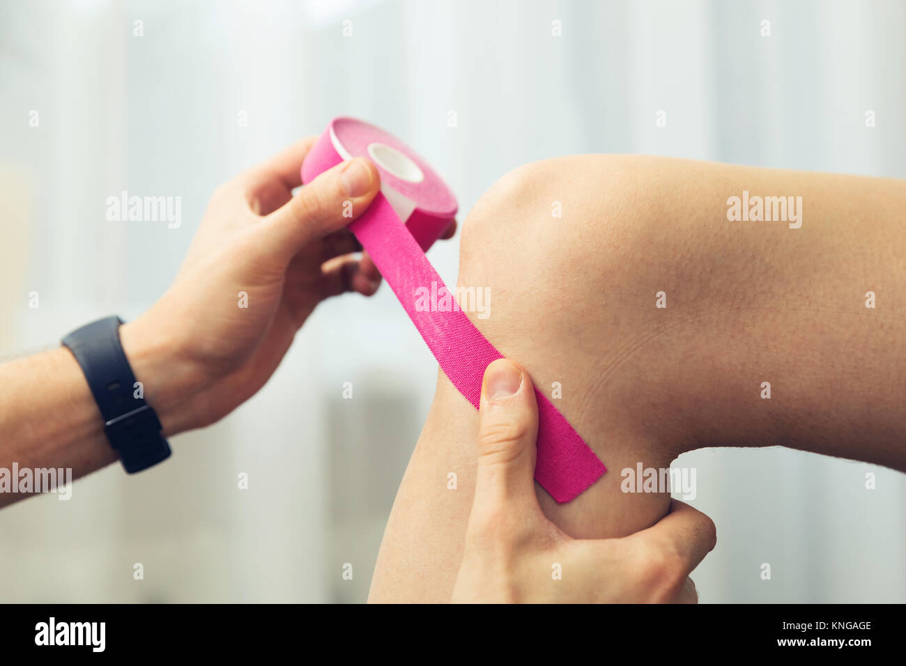 Lesiones deportivas - fisioterapeuta colocando cinta kinesio rosa sobre la  rodilla del paciente Fotografía de stock - Alamy