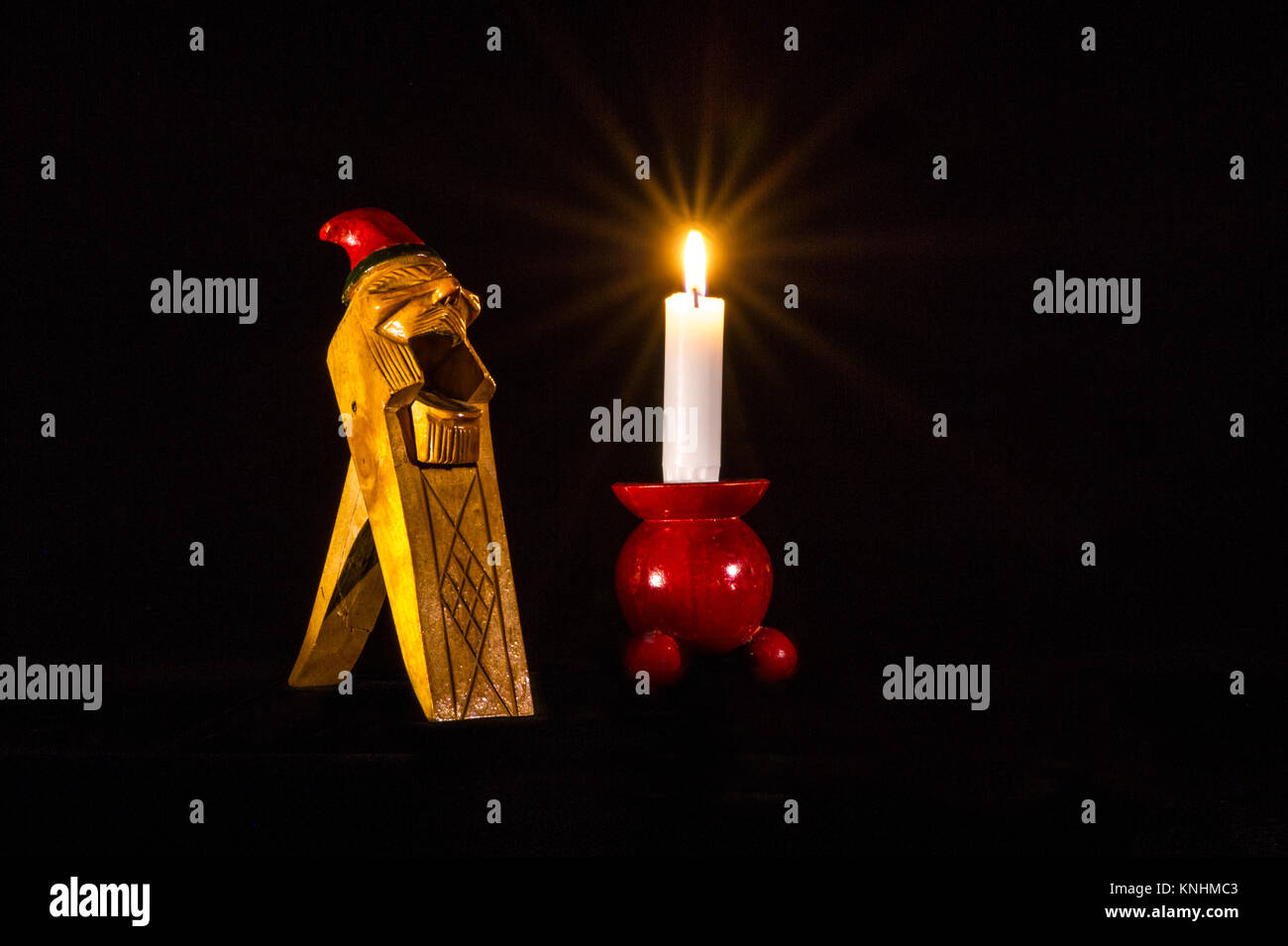 Un noruego Gnome Handcarved Cracker tuerca de madera junto con una luz de una vela en un candelabro de madera roja típica. Foto de stock