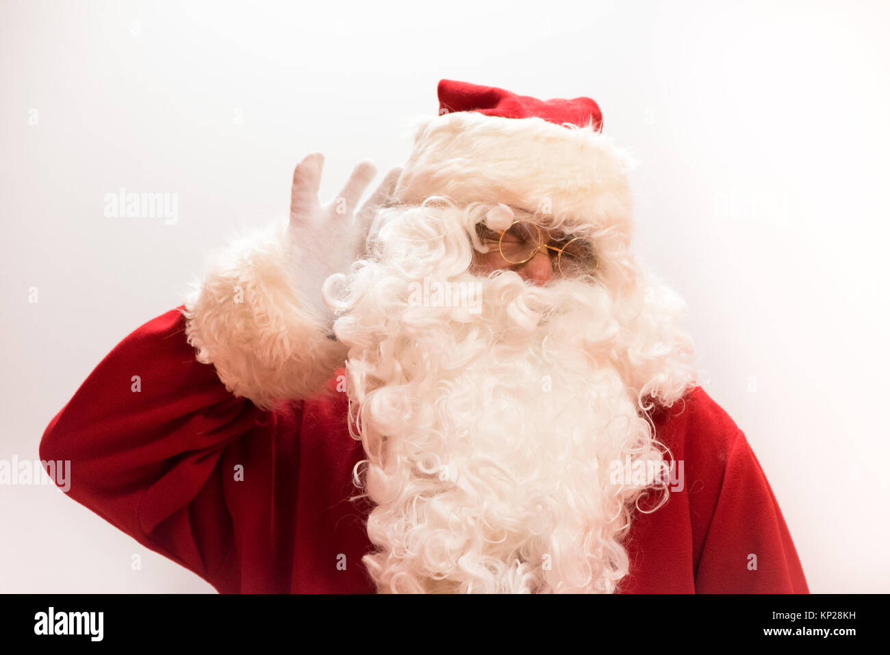 Santa Claus con la mano en el oído por el árbol de navidad. Aislados. Foto de stock