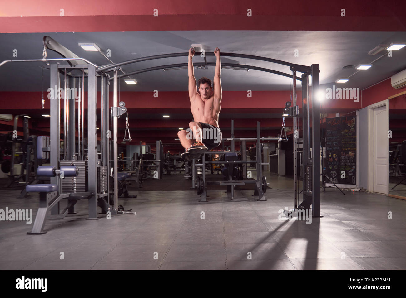 Un hombre joven, Gimnasio Multi-Station máquina abs ejercicio, gimnasio oscuro adentro, full lenght body shot. Foto de stock