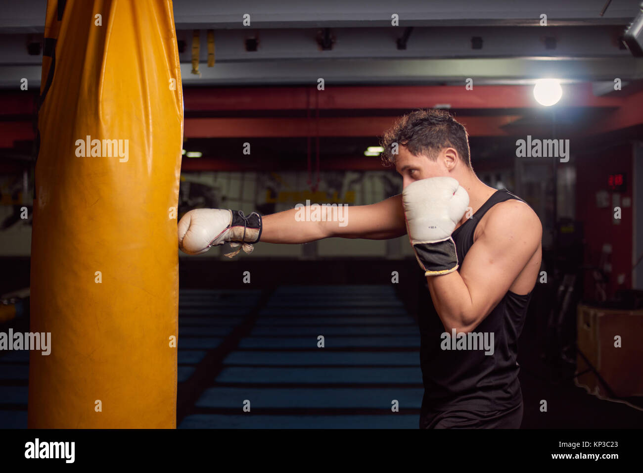 Un joven boxeador golpeando a mano saco de boxeo, practicando en interiores, sala de gimnasia, usando guantes de boxeo, disparos en la parte superior del cuerpo. Foto de stock