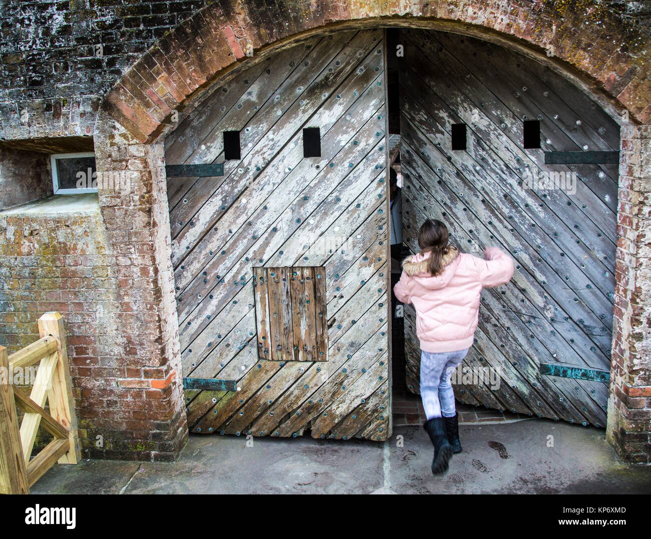Preadolescentes chica caucásica intentando empujar una pesada puerta de madera vieja en un antiguo fuerte. Fort Macon State Park, llamado originalmente, Fort Dobbs luego a Fort Macon Foto de stock