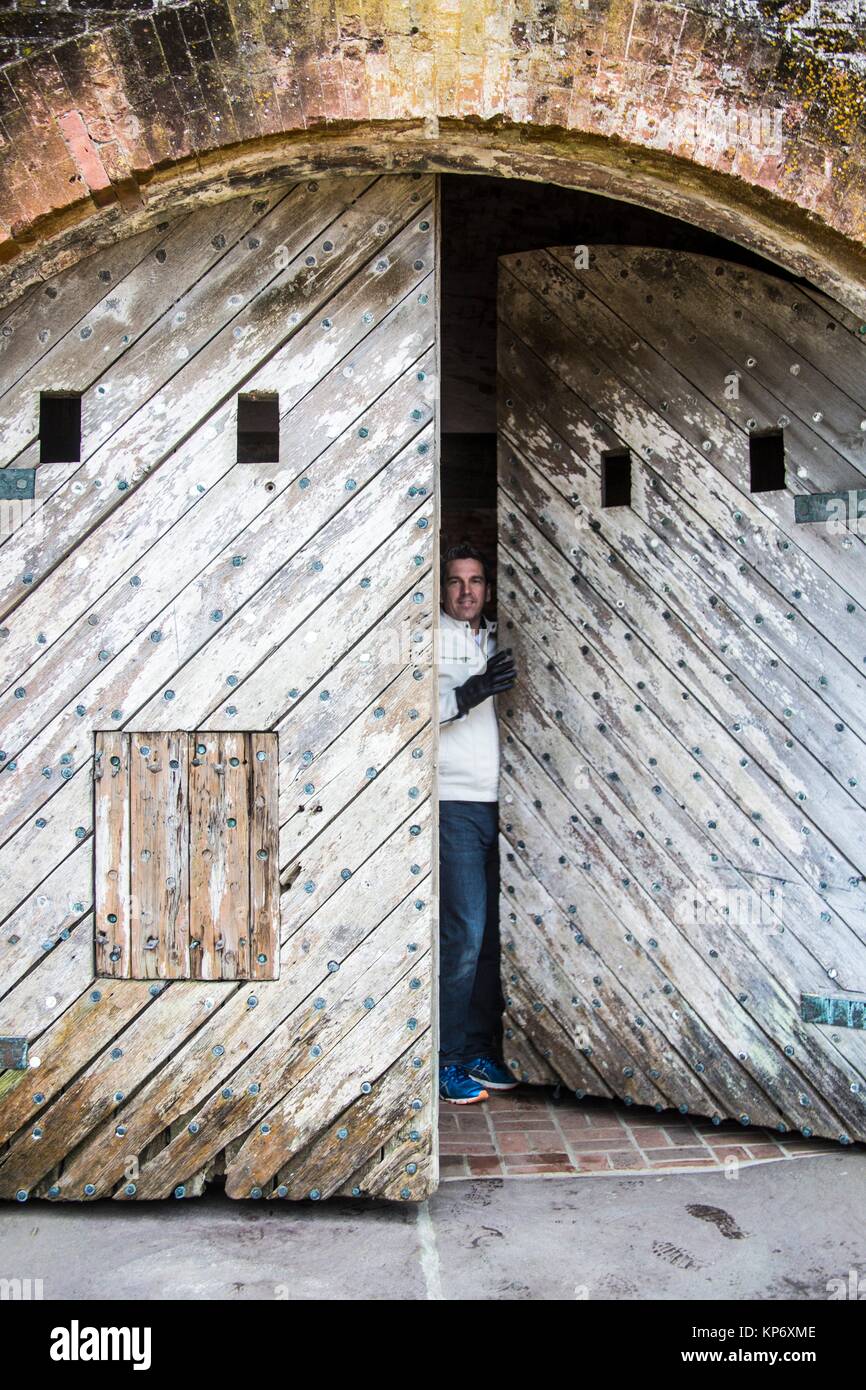 Caucasian guapo cabello oscuro hombre en sus 40's, 45's saliendo de un viejo fuerte madera antigua puerta de moda. Fort Macon State Park, llamado originalmente, Fort Foto de stock