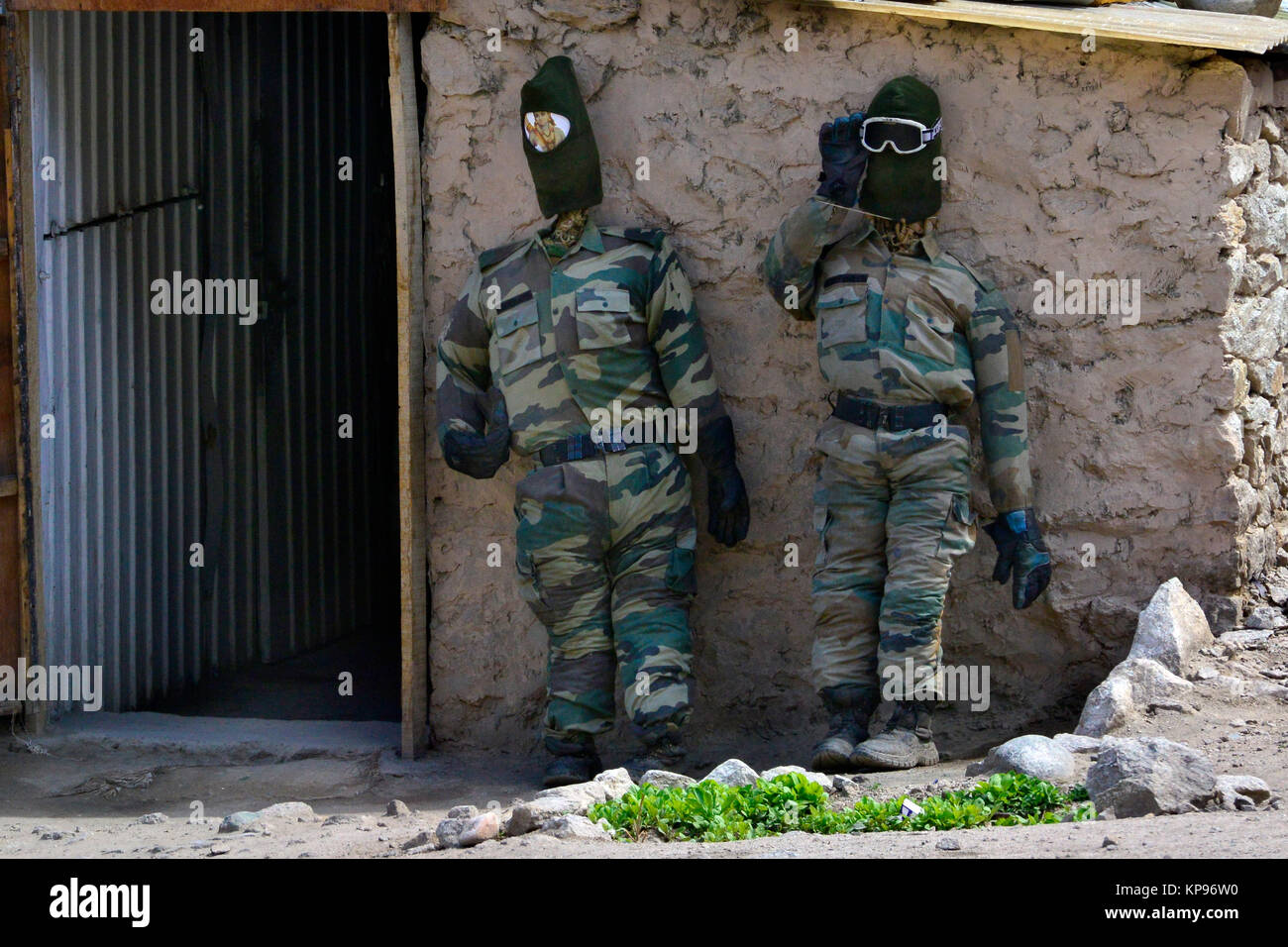 Dos muñecos de dummies militares en uniforme de camuflaje y máscaras  oscuras sobre sus cabezas, representan a los soldados de pie cerca de la  puerta de la casa de barro Fotografía de