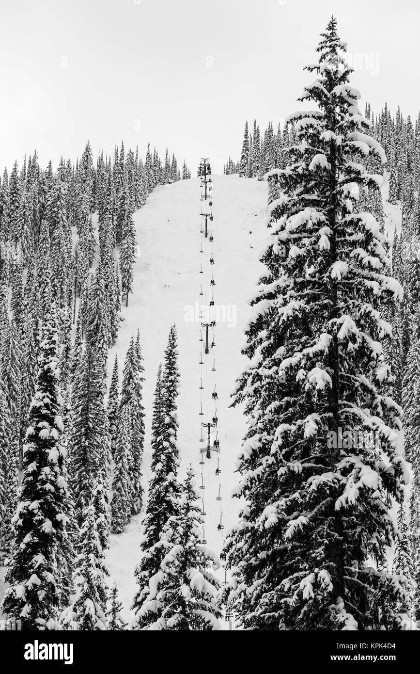 Un Telesilla sube por una empinada ladera de una colina de esquí cubierto de nieve en aguas bravas Resort; Nelson, British Columbia, Canadá Foto de stock