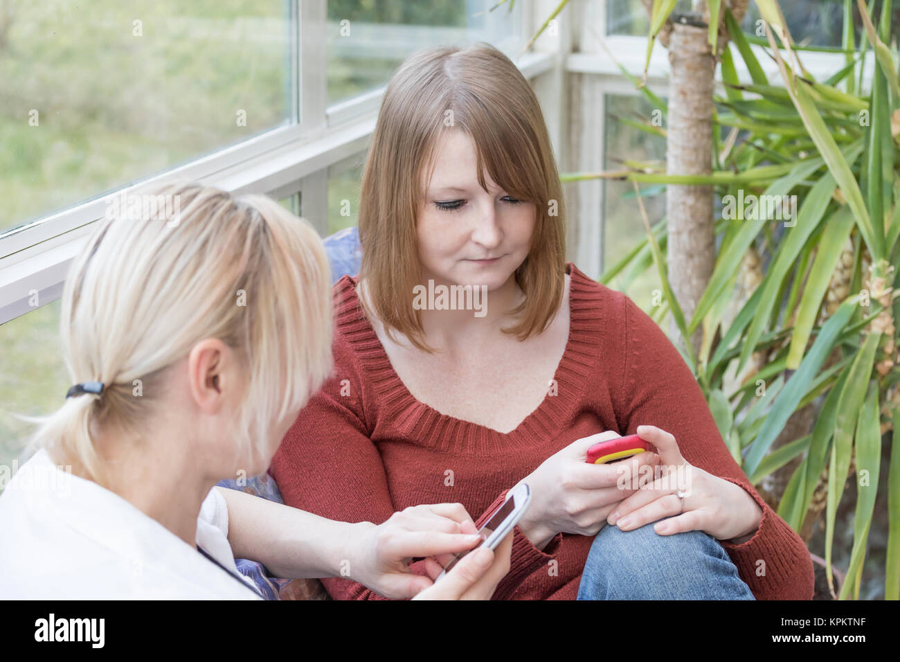Dos mujeres se encuentran buscando en su propio teléfono inteligente. Foto de stock