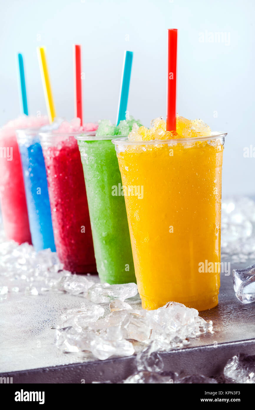 Still Life de colorida fruta congelada granizado Slush bebidas en plástico  para llevar tazas con pajas dispuestos en una fila sobre la superficie  metálica fría rodeado de cubitos de hielo Fotografía de