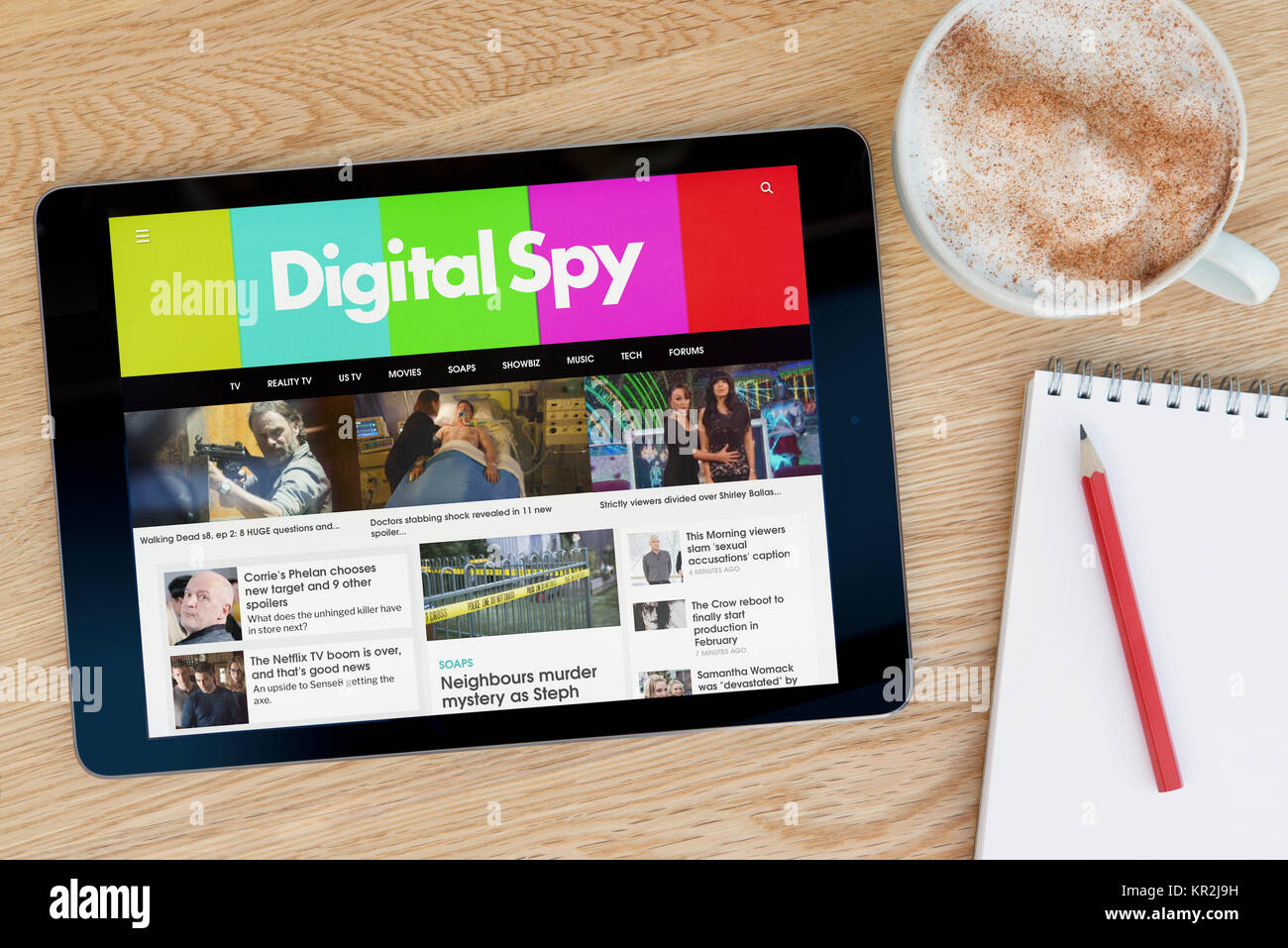 El sitio web Digital Spy en un dispositivo tablet iPad que descansa sobre una mesa de madera junto a un bloc de notas y lápiz y una taza de café (Editorial) Foto de stock