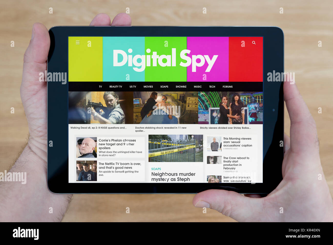 Un hombre se ve en el sitio web Digital Spy en su iPad dispositivo tablet, disparó contra una mesa de madera fondo superior (uso Editorial solamente) Foto de stock
