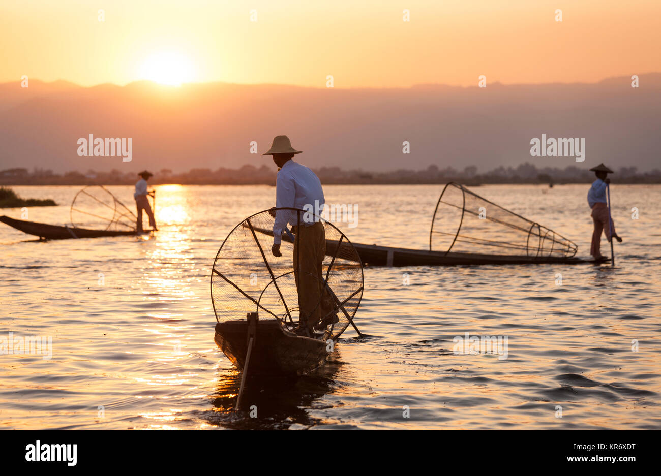 Pescadores tradicionales en un barco de pesca, sujetando el canasto, pesca en el lago al atardecer. Foto de stock