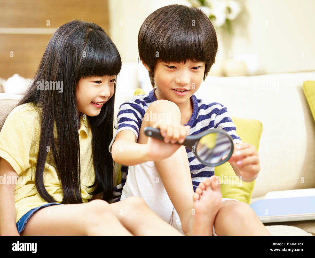 Dos niños asiáticos sentado en sofá en casa jugando con una lupa. Foto de stock
