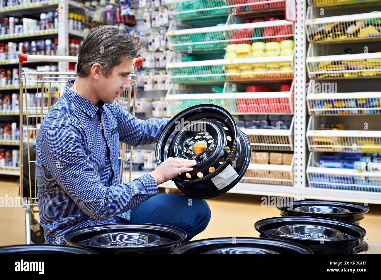 El hombre elige y compra los discos de metal con ruedas de un coche en una tienda. Foto de stock