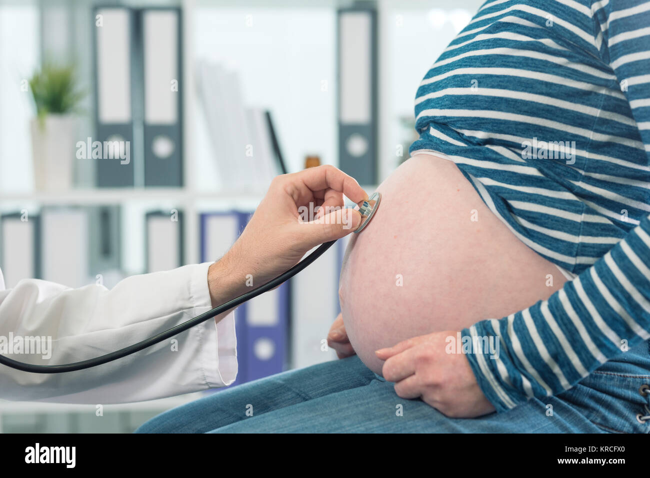 Médico examina la mujer embarazada con el estetoscopio. Control de salud durante el embarazo. Foto de stock