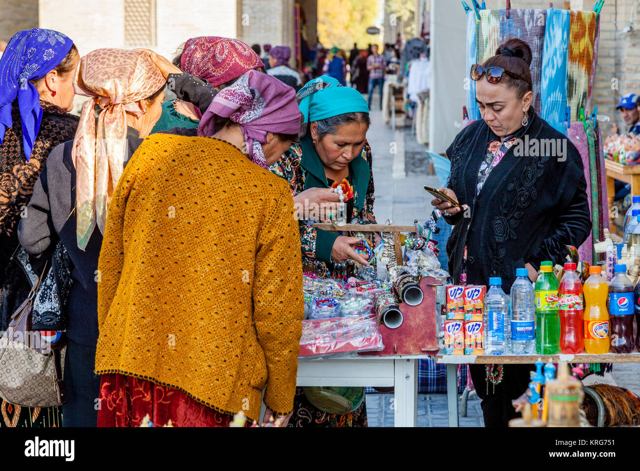 Un grupo de mujeres uzbekas Comprar artículos desde un puesto en el mercado, Bukhara, Uzbekistán Foto de stock