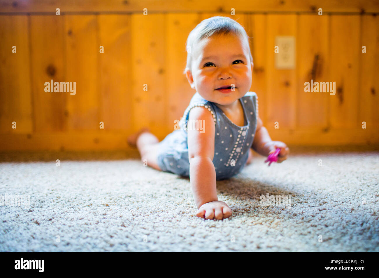 Sonriente niña de raza mixta arrastrándose sobre alfombra Foto de stock