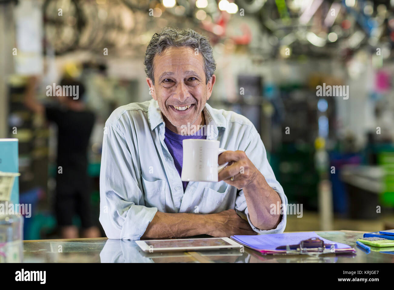 Retrato del hombre caucásico sonriente bebiendo café en la tienda de bicicletas Foto de stock