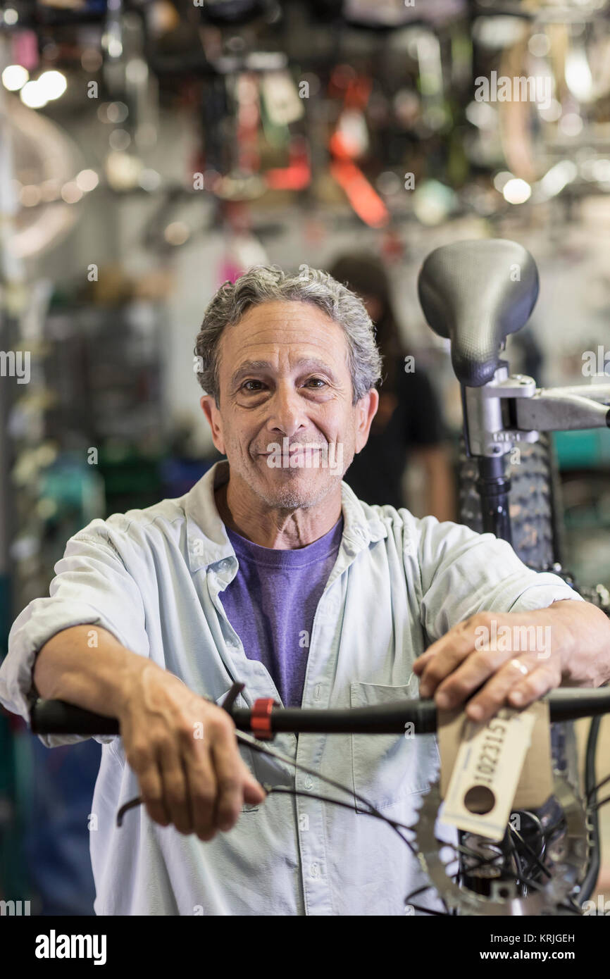 Retrato del hombre caucásico sonriente apoyado en bicicleta en la tienda Foto de stock