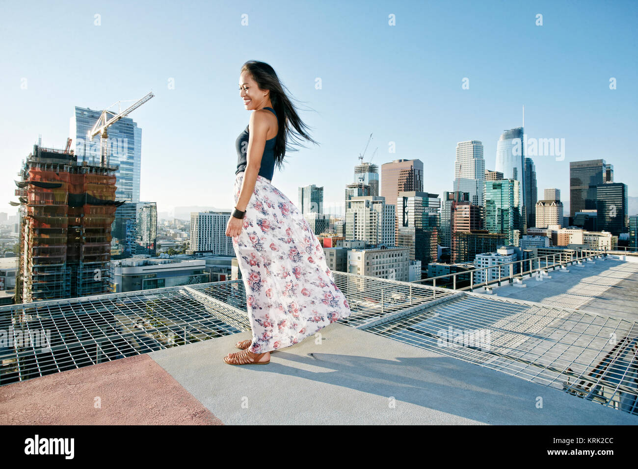Sonriente mujer asiática de pie en windy azotea urbana Foto de stock