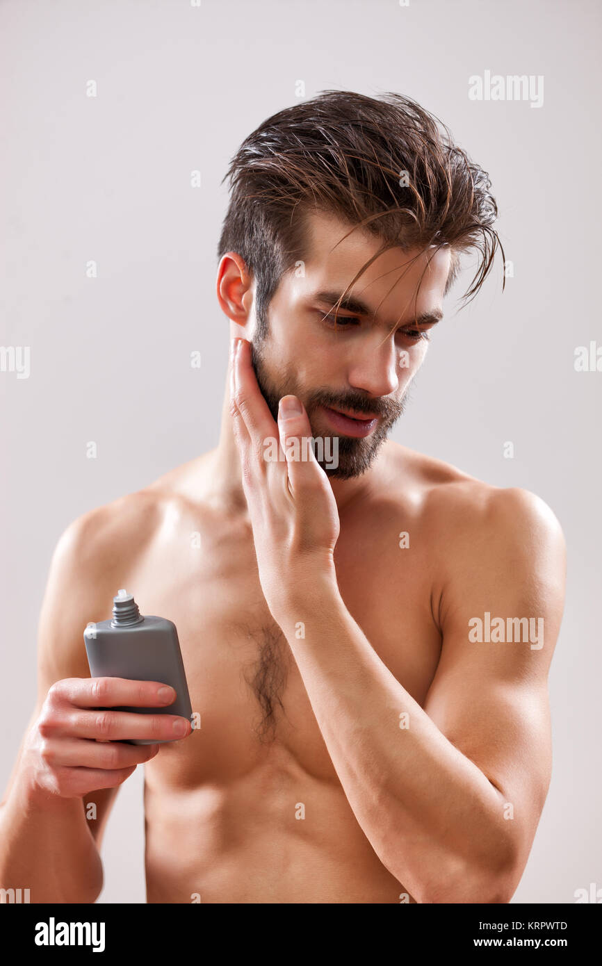Joven es aplicar lociones para después de afeitar a su cara. Foto de stock