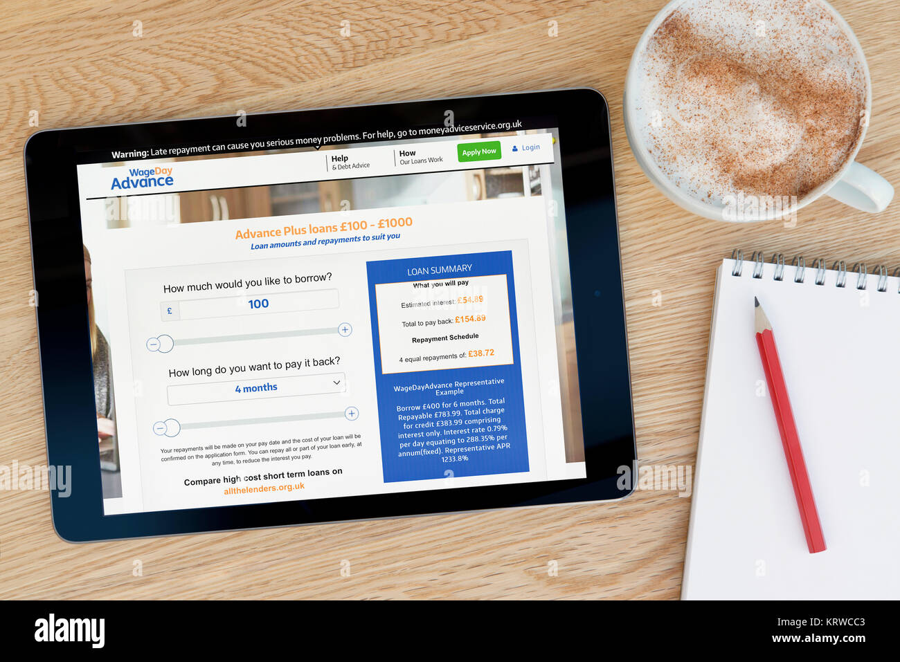 El salario días de anticipación en el sitio web de un dispositivo tablet iPad que descansa sobre una mesa de madera junto a un bloc de notas y lápiz y una taza de café (Editorial) Foto de stock