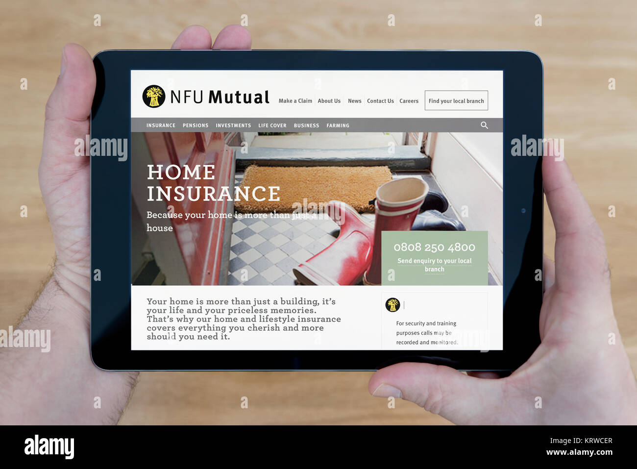Un hombre se ve en el sitio web de NFU Mutual en su iPad dispositivo tablet, disparó contra una mesa de madera fondo superior (uso Editorial solamente) Foto de stock