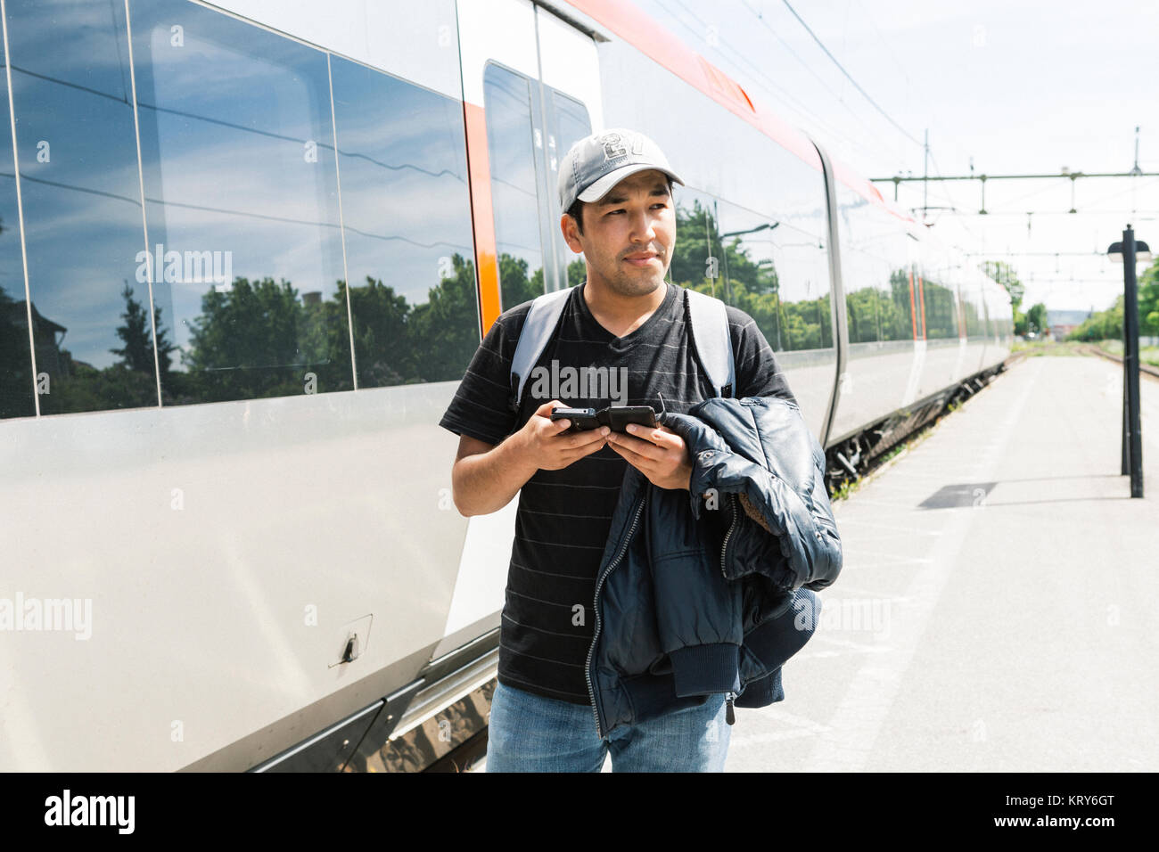 Hombre sujetando el teléfono inteligente en la plataforma de tren Foto de stock