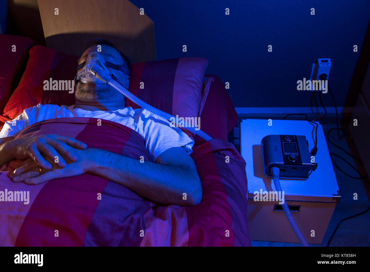 Un hombre con el síndrome de la apnea del sueño, lleva una máscara de CPAP mientras duerme, máscara respiratoria que comprime el aire en las vías respiratorias por sobrepresión, evitando vías respiratorias Foto de stock