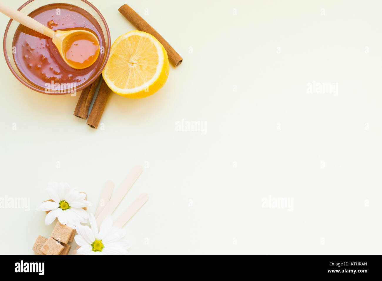 Depilación de azúcar o de fondo para el cuidado de la piel- un cuenco de  miel con una cuchara de madera, un fresco de limón, flores de manzanilla,  cubos de azúcar marrón,