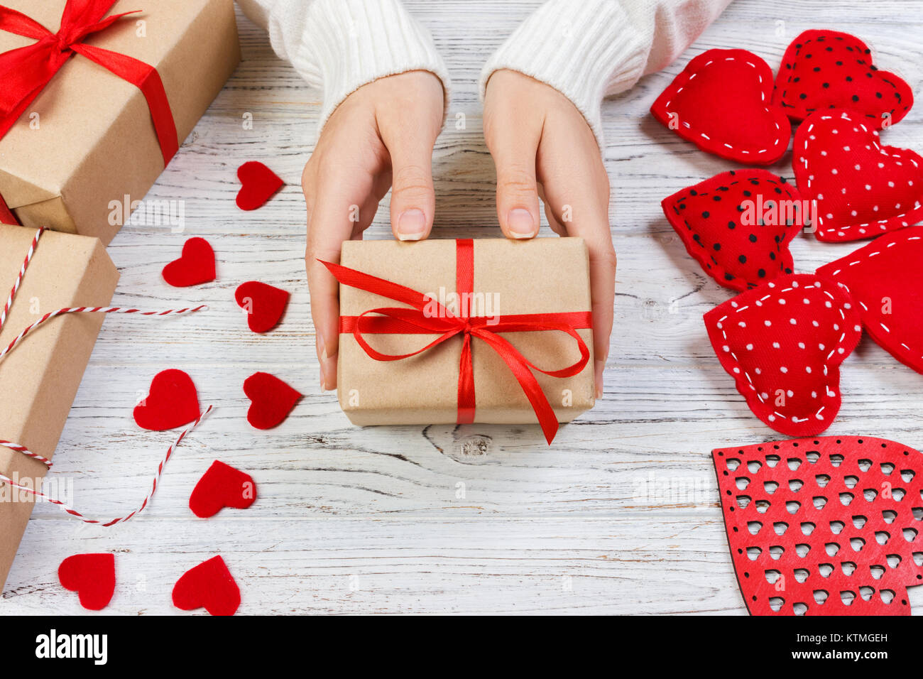 Mano femenina sosteniendo un regalo para el Día de San Valentín, un  cumpleaños o el día de la madre. Romántico fondo de madera blanca con  corazones y regalos. Sentar planas Fotografía de