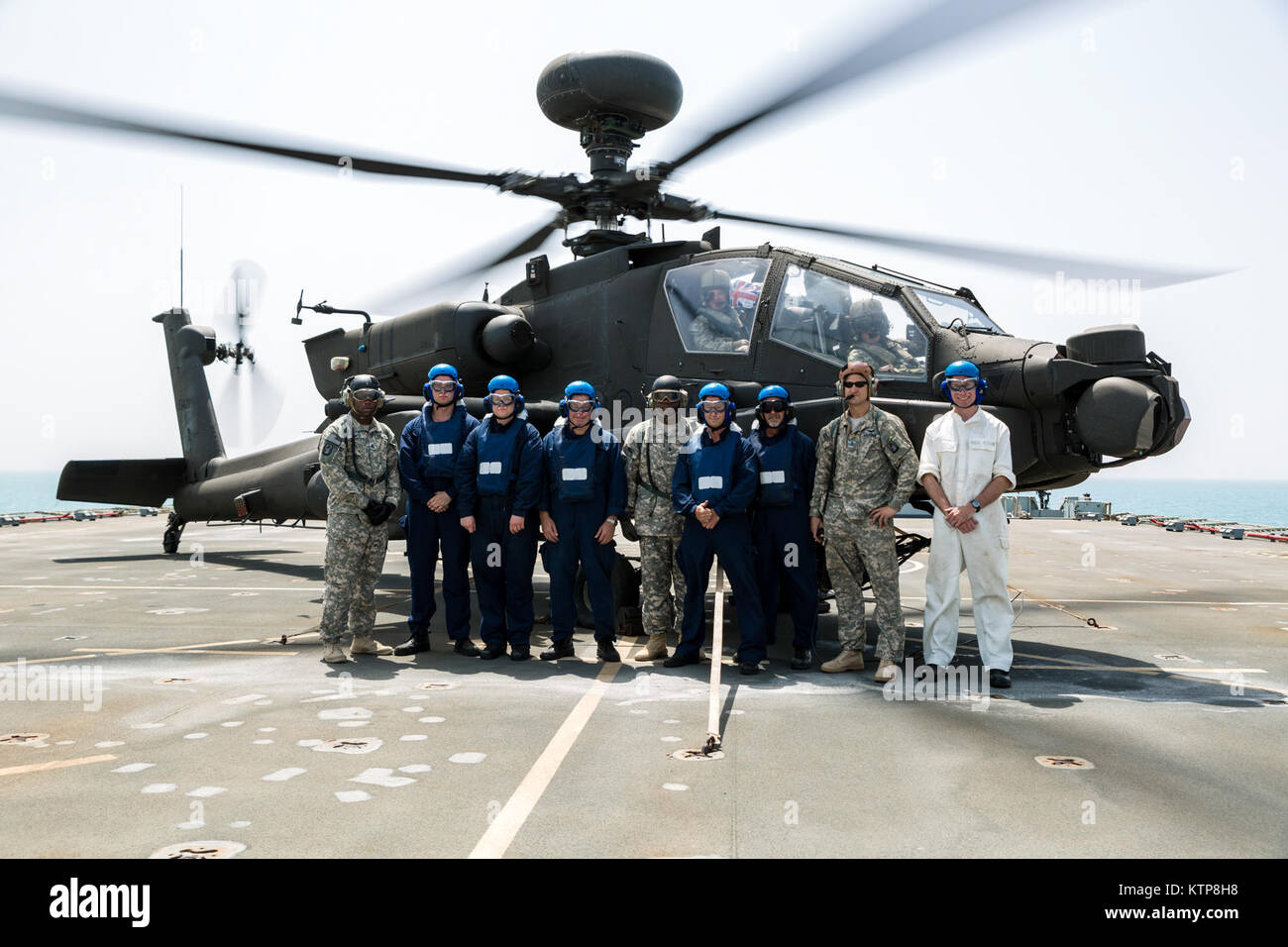 La tripulación de cubierta de la RFA Cardigan Bay, auxiliar de la flota Real, en el Reino Unido, la Royal Navy, párese frente a un Apache AH-64 volados por los pilotos del 3º Batallón, 159ª Batallón de reconocimiento de ataque, la 42ª Brigada de Aviación de Combate (Cabina) del Ejército de Estados Unidos, el 10 de junio de 2014, en algún lugar en el Golfo Arábigo. El Apache pilotos entrenados en la cubierta de los desembarques y funcionó como Scouts para el Cardigan Bay durante el ejercicio Kopis espartano, un intercambio entre el Cardigan Bay y tanto el Black Hawk y Apache AH-64 elementos de la cabina, 42 de la Guardia Nacional del Ejército de Nueva York. Spartan Kopis era la primera vez que American Apaches trabajó w Foto de stock