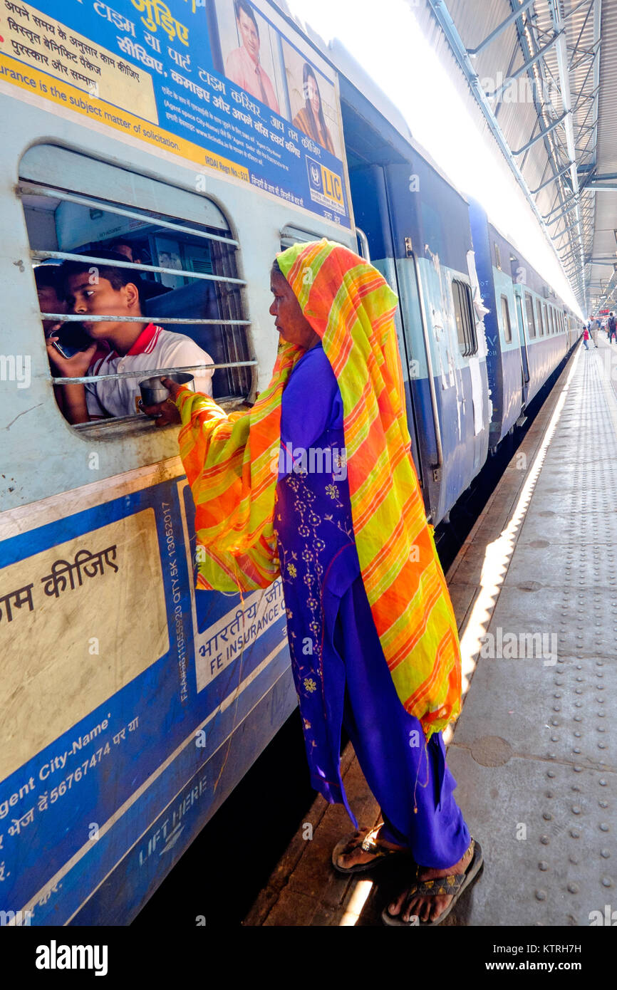 Mujer india la mendicidad a través de la ventana del tren. Jóvenes en el teléfono del pasajero ignora su Foto de stock