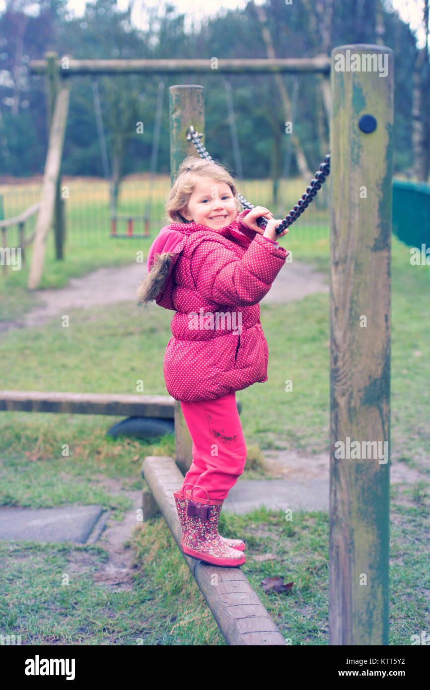 Chica de pie sobre una viga de equilibrio de madera en un parque infantil Foto de stock