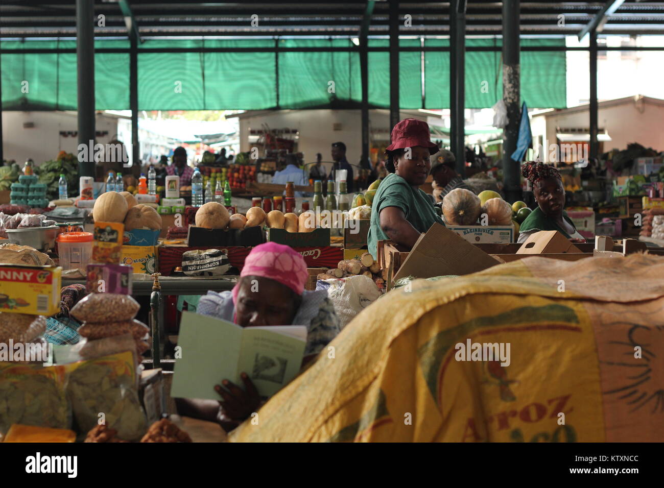 Las mujeres en un tradicional mercado urbano de Maputo, Mozambique vendiendo productos diversos y una mujer en la primera lectura de un libro. Foto de stock