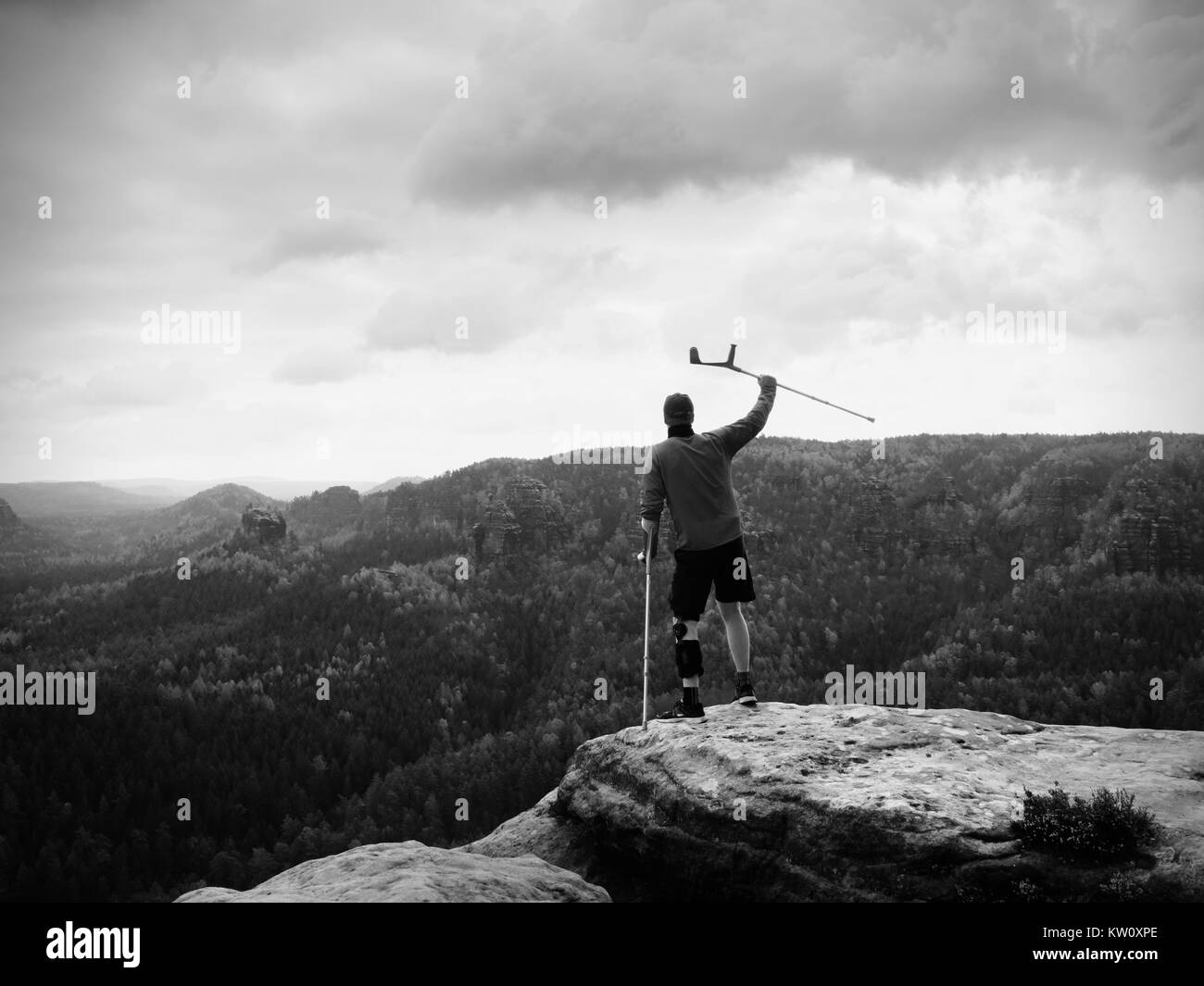 Hombre con muletas de antebrazo. Caminante finaly alcanzado el pico de la montaña. Turista con la pierna rota en el inmovilizador mantenga medicamento polacos. Foto de stock