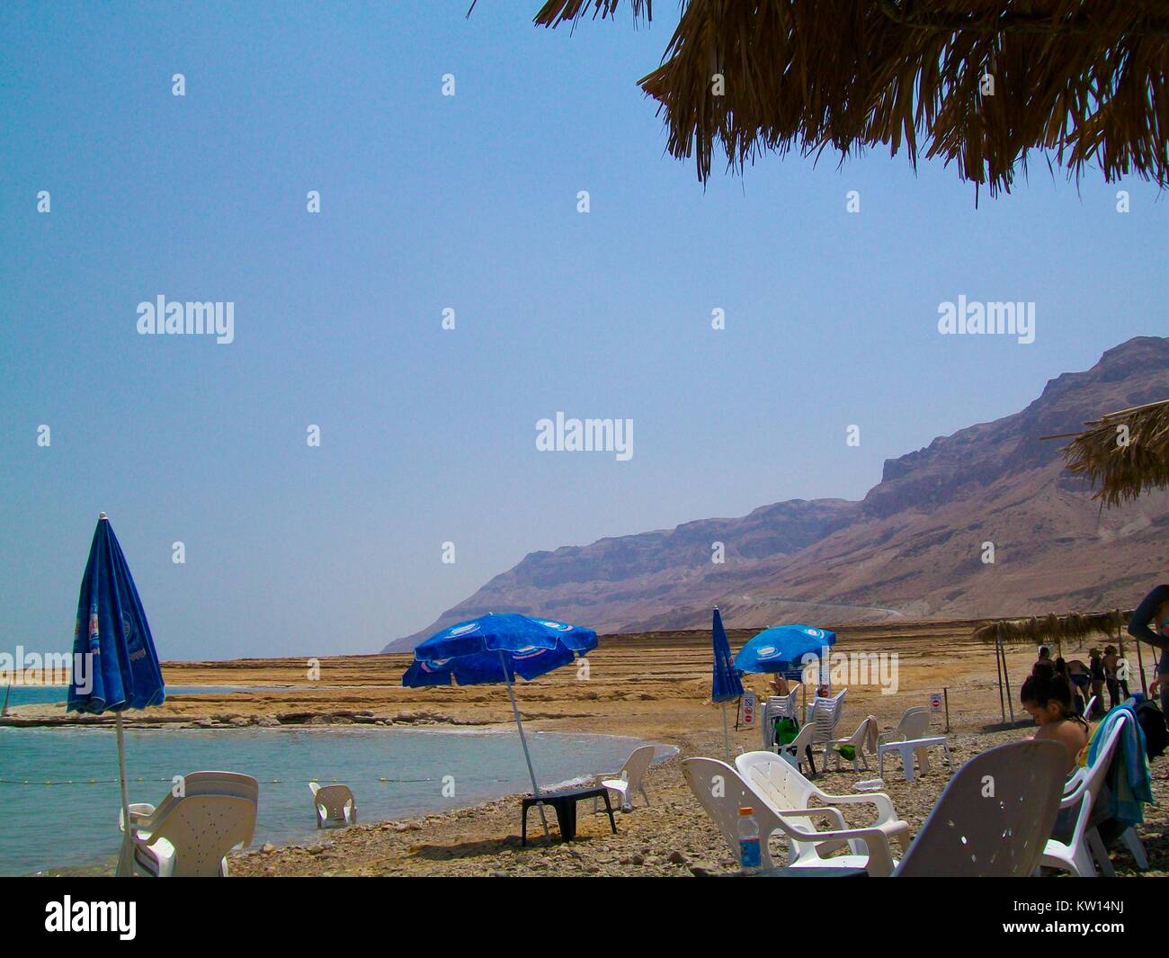 Los turistas relajarse en reposeras de plástico bajo el paraguas de la marca Nestlé cerca del Mar Muerto, Israel, 2012. Foto de stock