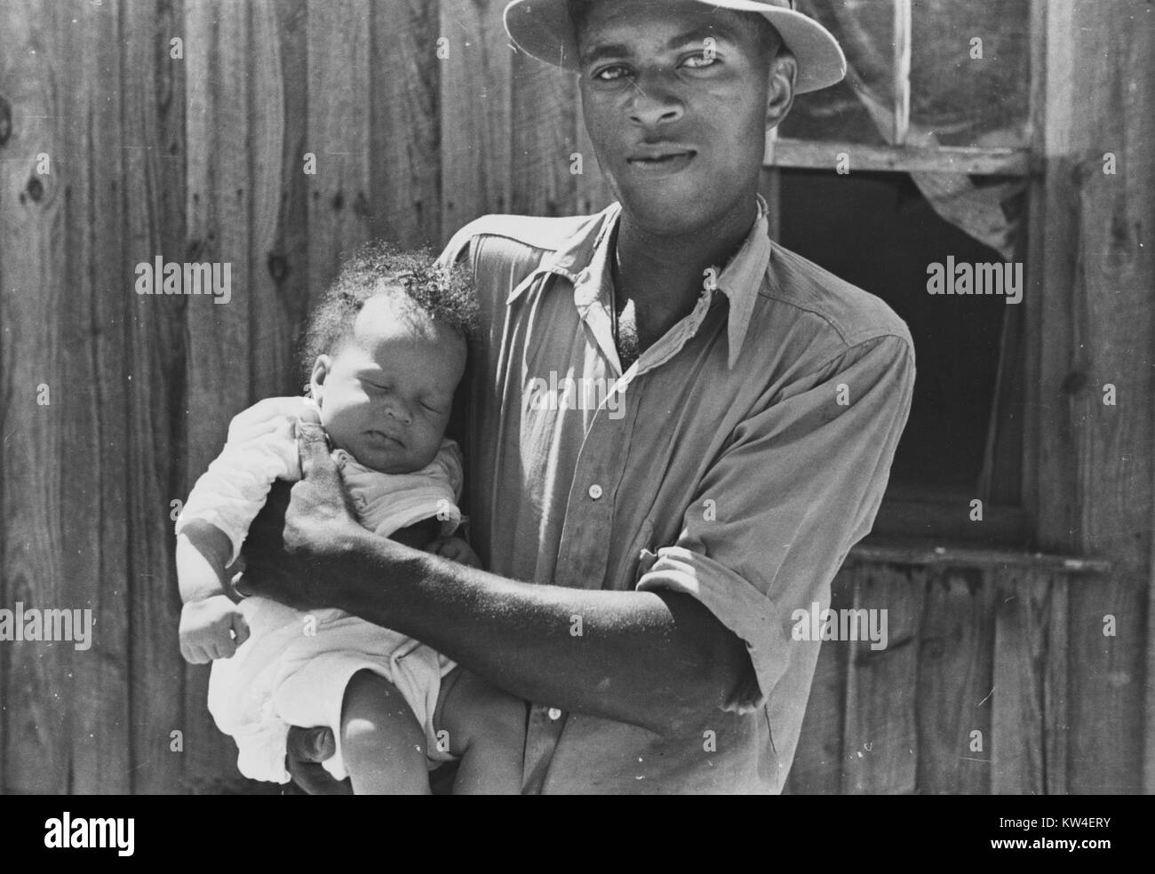 El arrendatario usando un botón de la camisa y un sombrero tiene a su joven hijo, en Lee County, Mississippi, agosto de 1935. Desde la Biblioteca Pública de Nueva York. Foto de stock