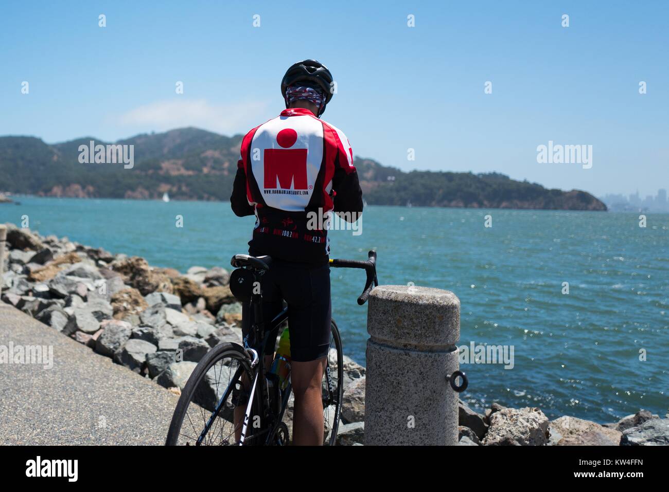 Un ciclista paradas a lo largo del muelle en Tiburon, California y tiene vistas a la bahía de San Francisco hacia San Francisco, 2016. Foto de stock