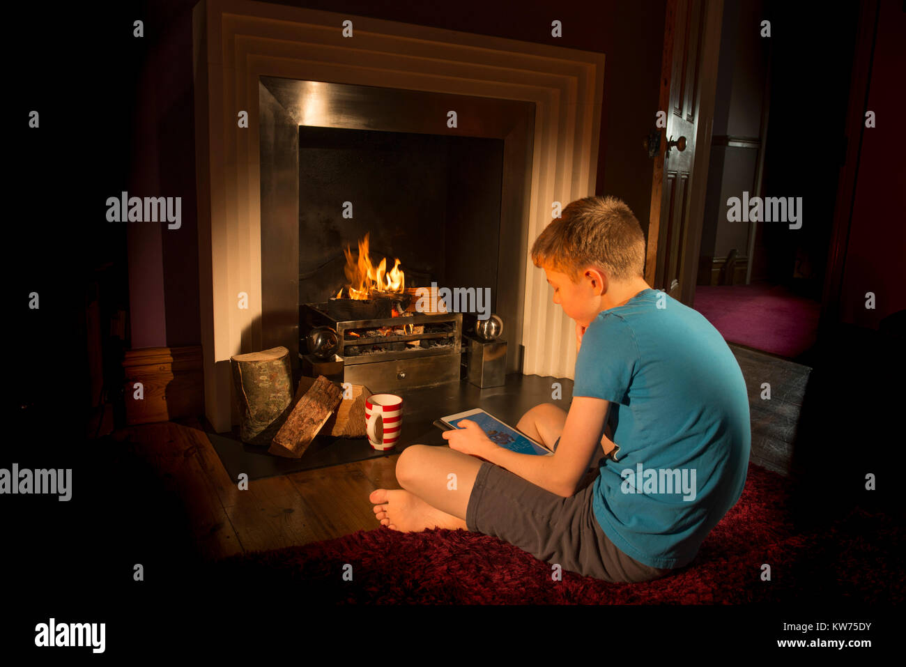 Adolescente mirando tableta en frente del fuego. Hygge Foto de stock