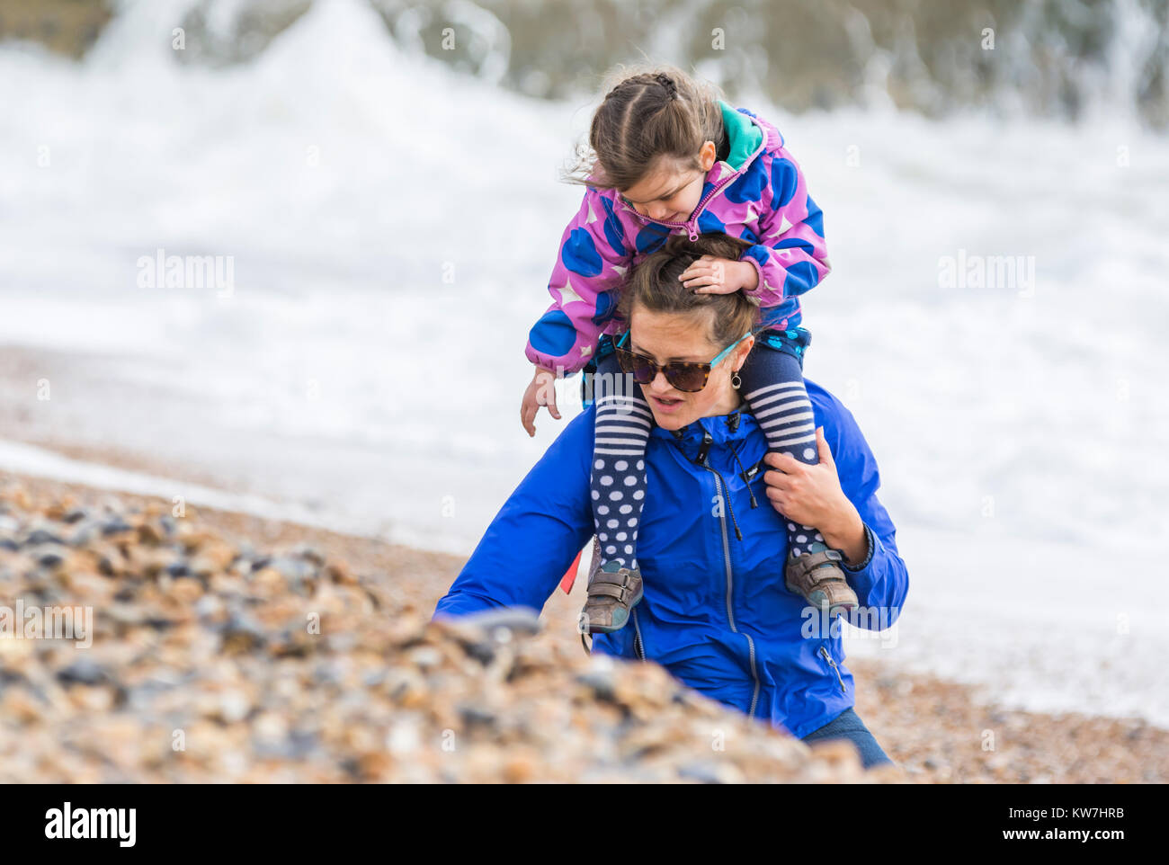 Niño sobre los hombros de las mujeres recoger conchas en la playa en una dura jornada en el Reino Unido. Foto de stock