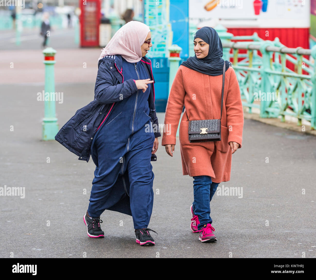 Pareja de mujeres, probablemente musulmana debido a la ropa, usando un hijab caminando mientras habla en Brighton, East Sussex, Inglaterra, Reino Unido. Foto de stock