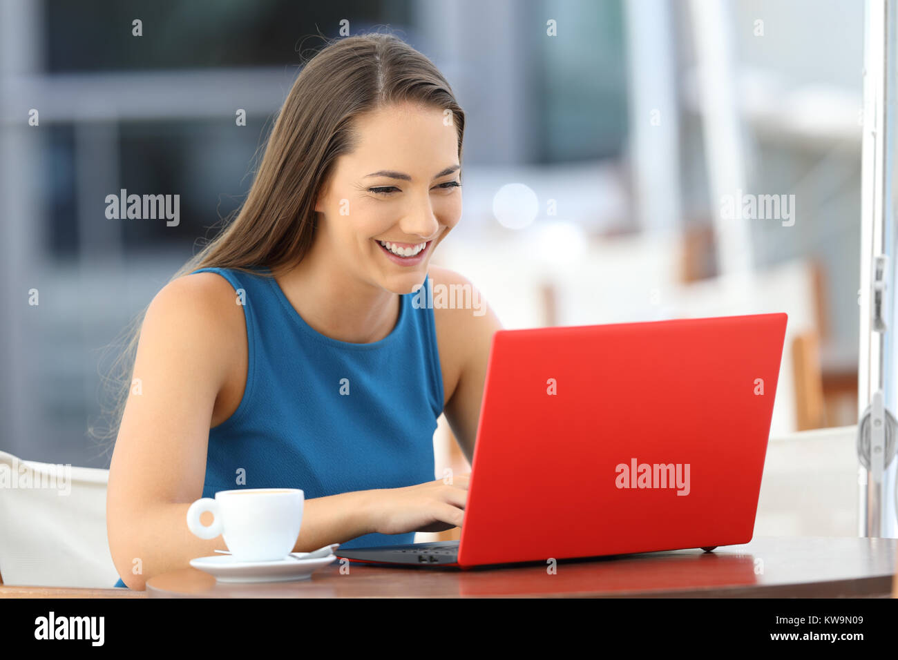 Mujer feliz escribiendo en un solo equipo portátil rojo sentado en un bar terraza Foto de stock