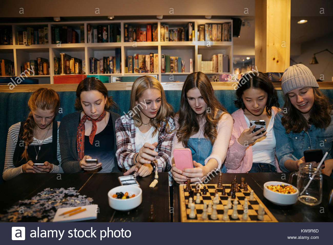 Tween amigas sentada en una fila,mensajes de texto con teléfonos inteligentes y jugar al ajedrez en el café la tabla Foto de stock